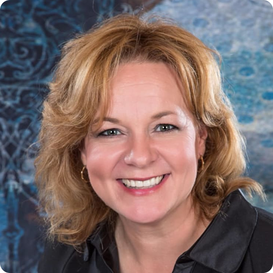 A woman with shoulder-length blonde hair and a black blouse smiles at the camera. The background features a blue and patterned design.