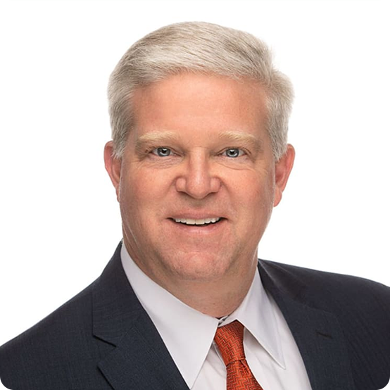 A middle-aged man with short gray hair, wearing a dark suit, white dress shirt, and orange tie, smiling and posing against a plain white background.