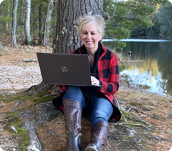 A woman sits on a tree trunk with her laptop, planning her next business expansion amid nature’s tranquility.